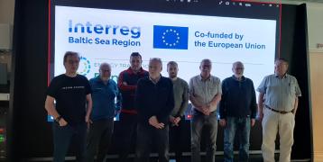 Participants of collaboration forum meeting Eight persons standing in the front of office screen